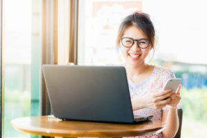 Pretty young happy asian woman laughing while holding smartphone.