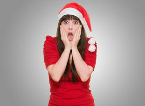 scared woman wearing a christmas hat against a grey background